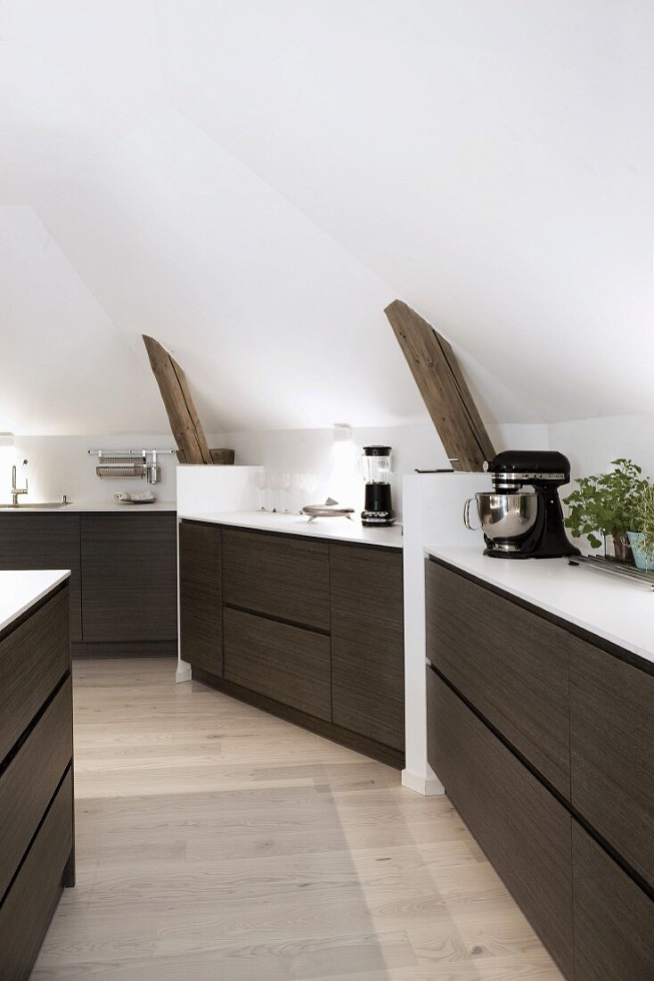 Custom kitchen counter with dark wooden drawer fronts fitted against sloping attic walls