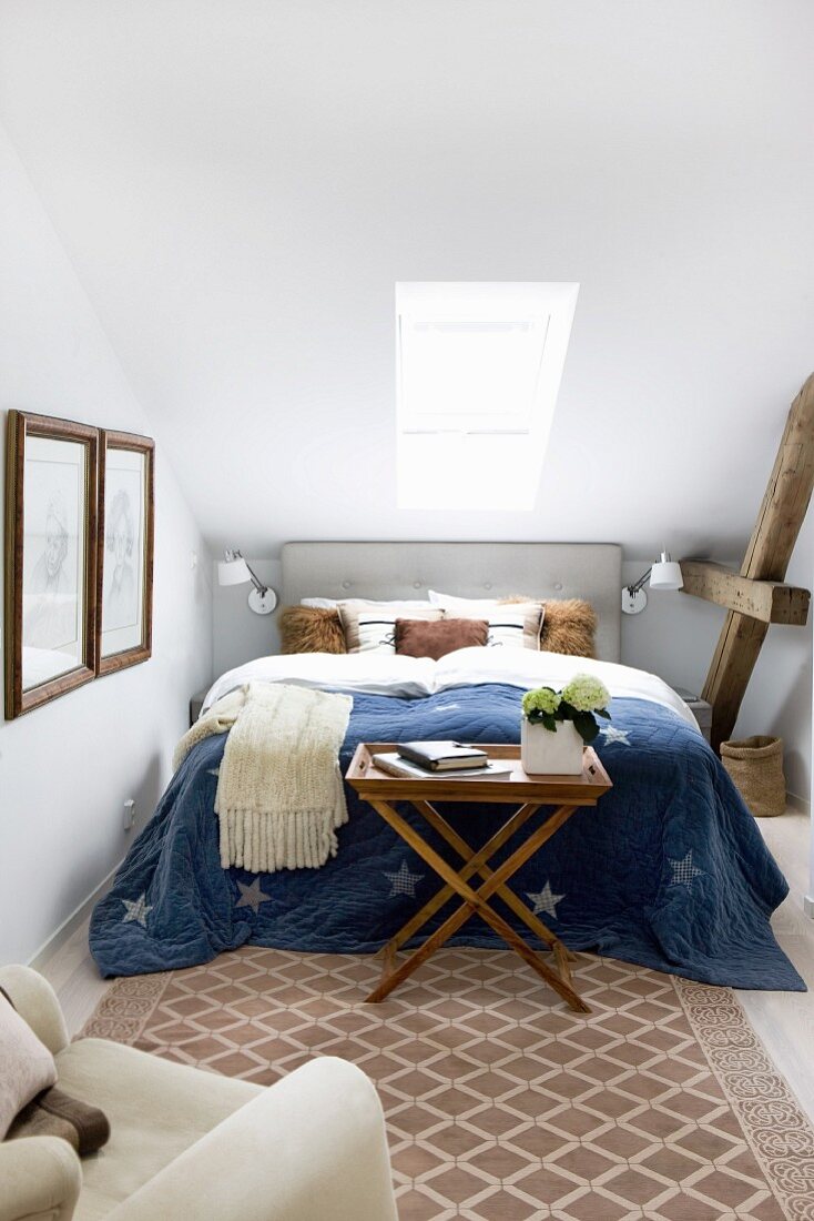 Blue bedspread on double bed below skylight in narrow bedroom