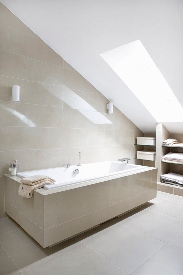 Bathtub in modern attic bathroom with sand-coloured tiles