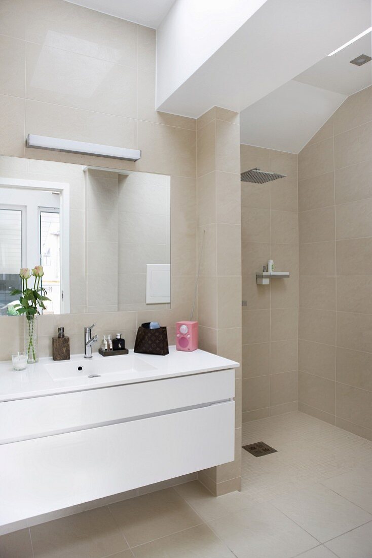 Modern washstand with white base unit against beige-tiled wall next to floor-level shower