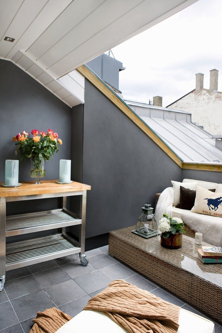 Loungebereich mit Rattanmöbeln auf Dachterrasse, seitlich Teewagen