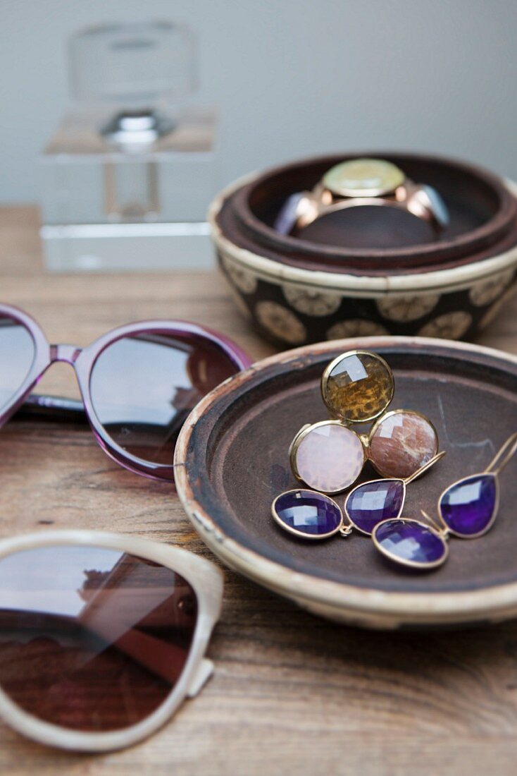 Sonnenbrillen und Damenschmuck in Keramiksschalen auf Holztisch