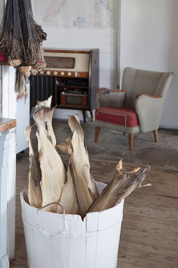 Getrocknete Fische in geweisseltem Holzzuber, im Hintergrund Fifties Sessel in rustikalem Ambiente
