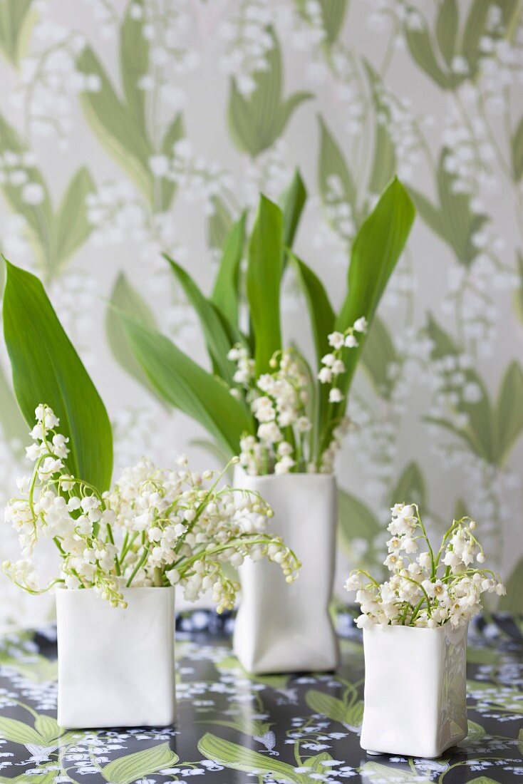 Lily of the valley in designer vases in front of wallpaper with lily of the valley pattern