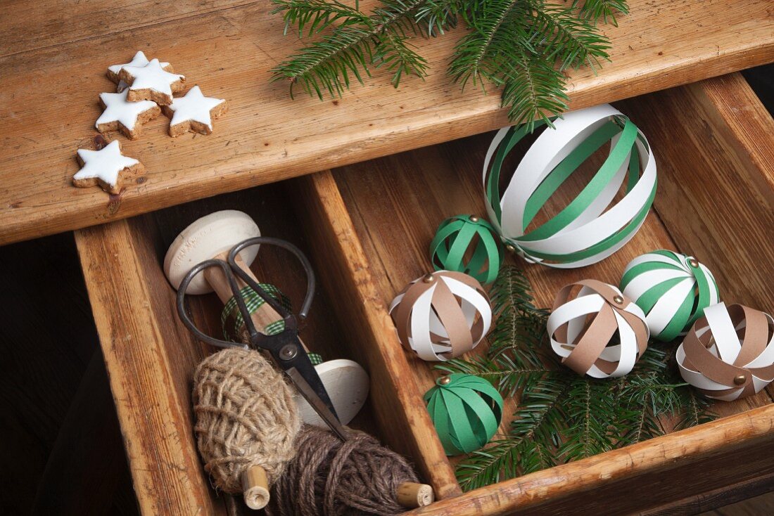 DIY-Dekobälle aus Papierstreifen und gewickelte Seile in hellen Brauntönen, weihnachtlich arrangiert mit Tannenzweigen und Zimtsternen
