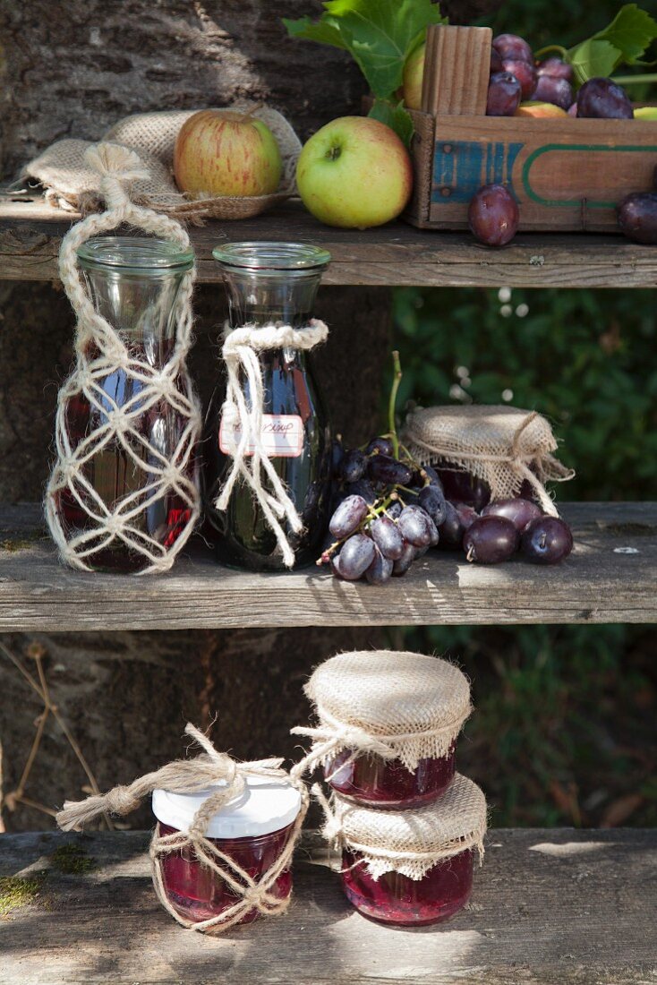 Flaschen und Marmeladengläser mit Makramee-Dekoration auf verwittertem Holzregal zur Erntezeit