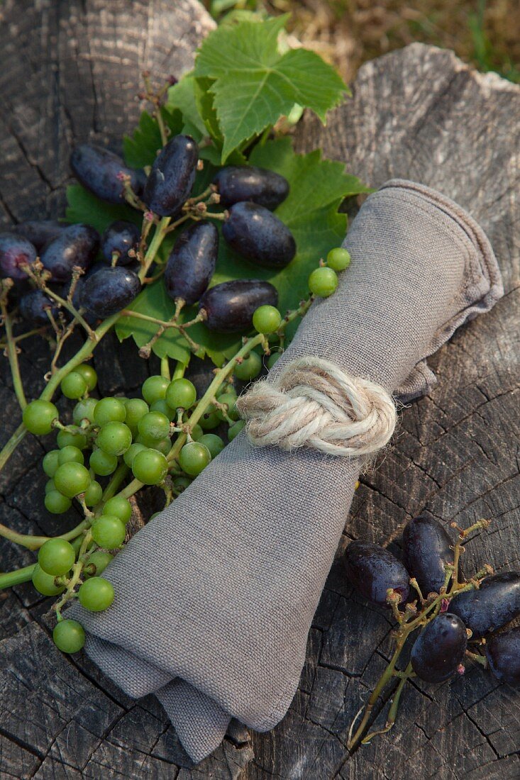 Leinenserviette mit einem Achterknoten aus Juteschnüren zusammengebunden neben geernteten Trauben