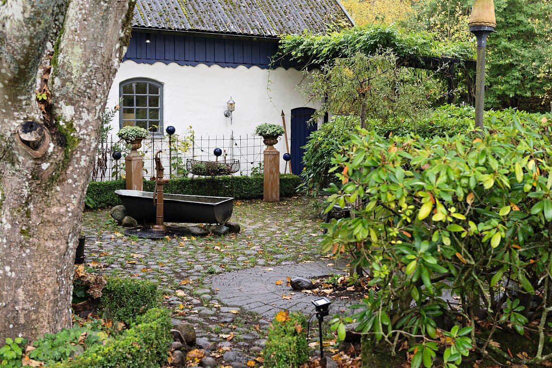 Vintage Zinkwanne auf Kieselsteinboden, vor weiss gestrichenem Landhaus im Garten