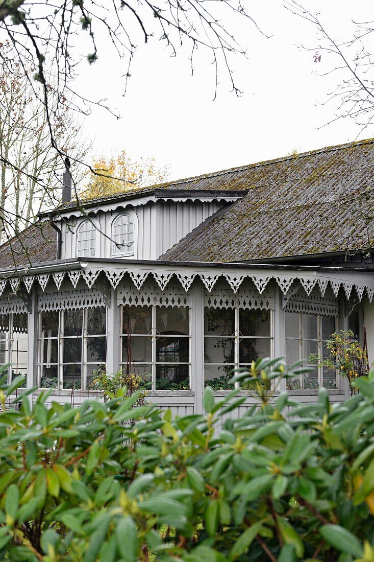 View from garden of house with conservatory and grey-painted, carved wooden trim on eaves