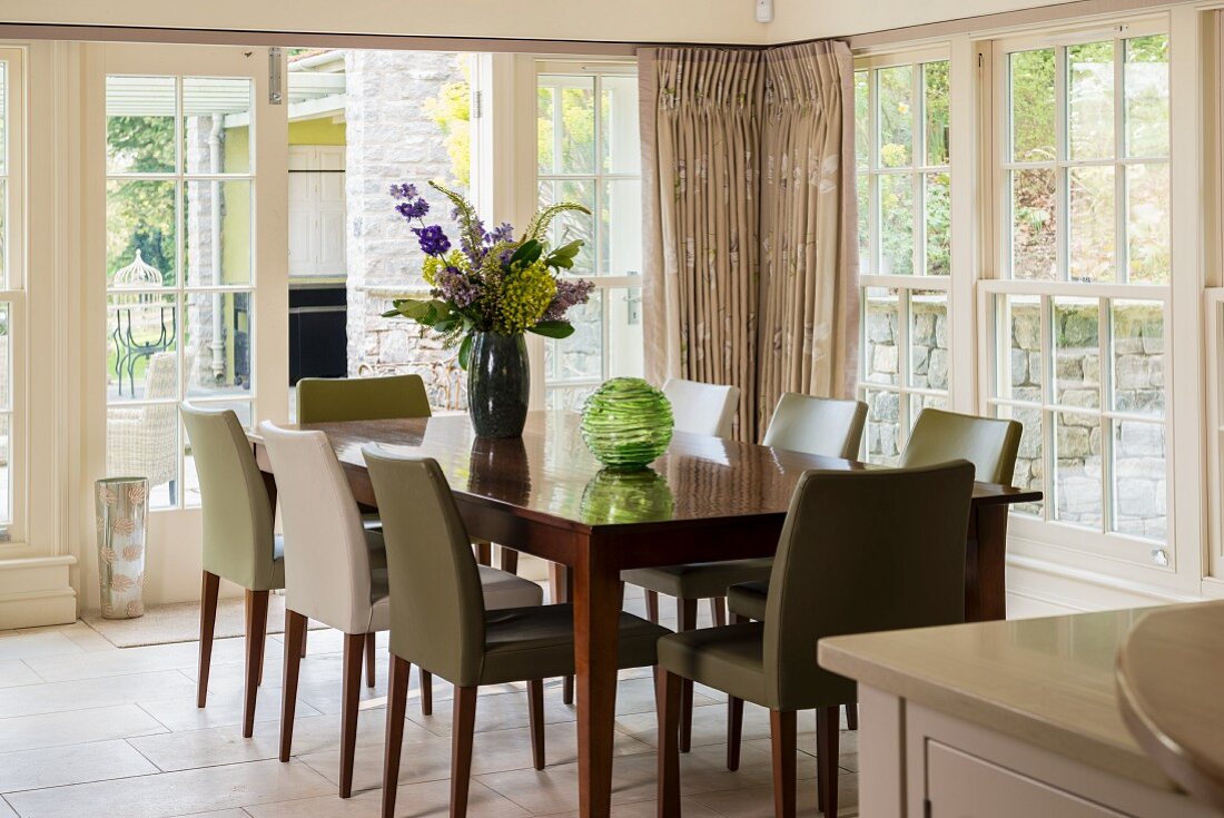 Dining area in conservatory with lattice windows, wooden table and upholstered chairs with various covers
