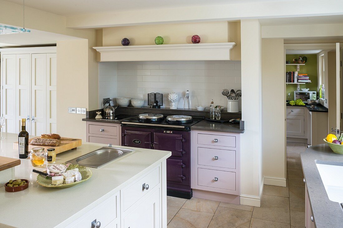 Island counter and classic cabinets with doors in various pale shades in open-plan kitchen