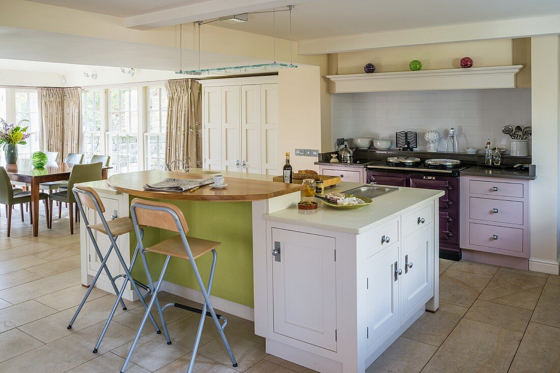 Island counter and classic cupboard doors in various colours in open-plan kitchen with dining area in background