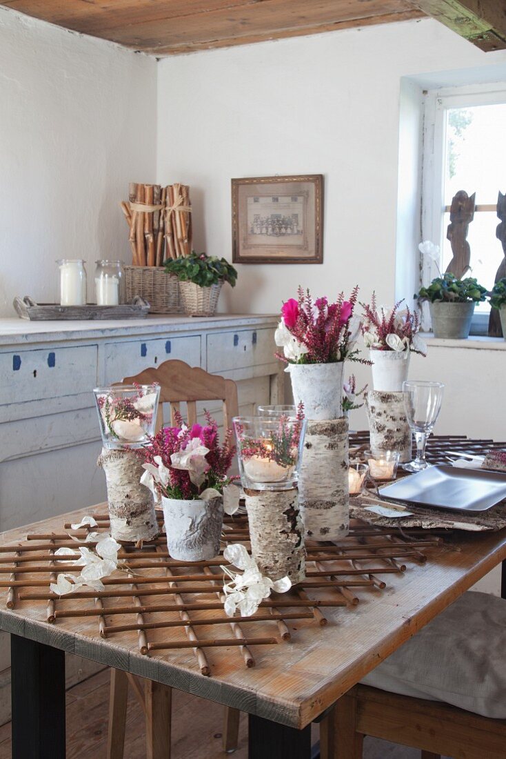 Mit Naturmaterialien dekorierte Vasen und Blumengestecke auf rustikalem Tisch in bäuerlichem Esszimmer