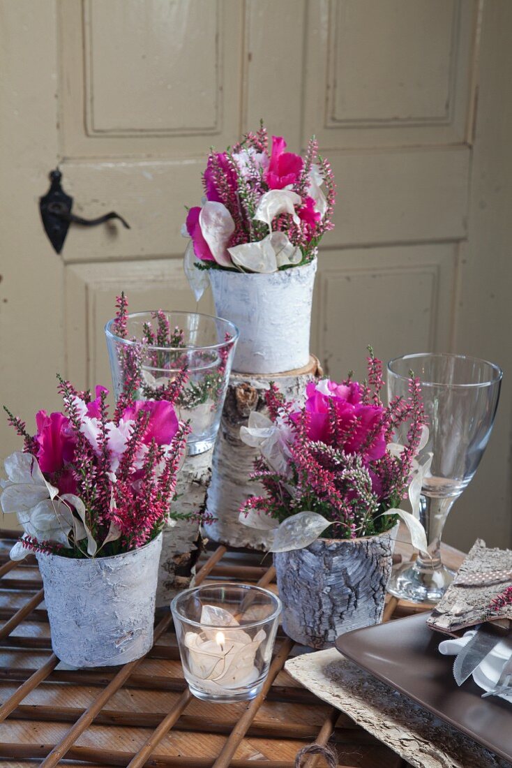 Romantische Blumengestecke mit pinkfarbenen Alpenveilchen, Calluna und Silberblatt in Vasen mit Birkenrinde