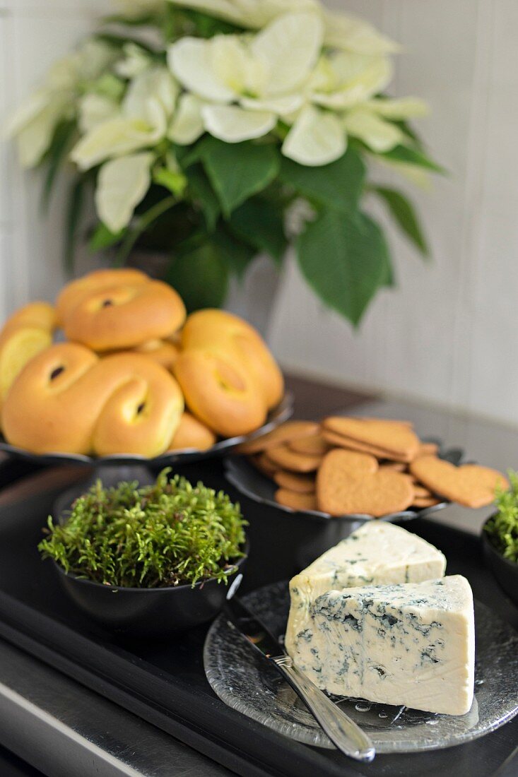 Biscuits, pastries and blue cheese on black tray in front of white poinsettia