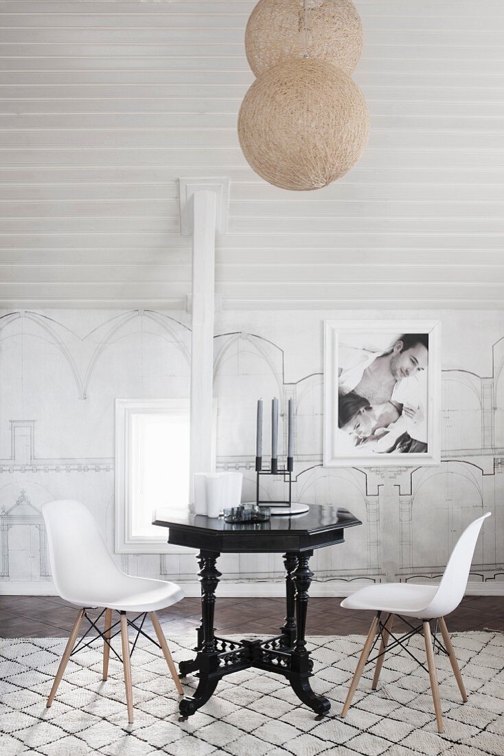 Classic chairs with white shell seats at black, vintage-style table below spherical pendant lamps suspended from ceiling