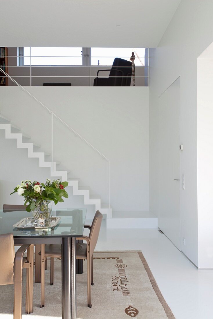 Modern table with glass top in dining area in front of staircase with minimalist handrail