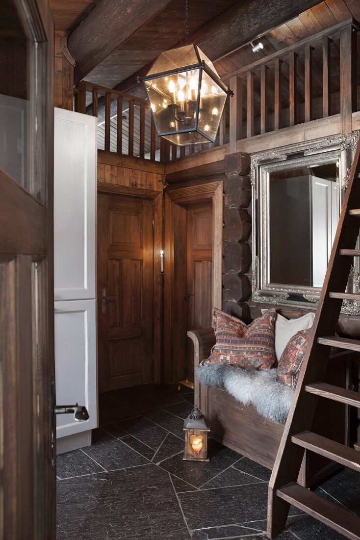 Lantern-style lamp in foyer of log cabin with cloakroom bench below mirror to one side