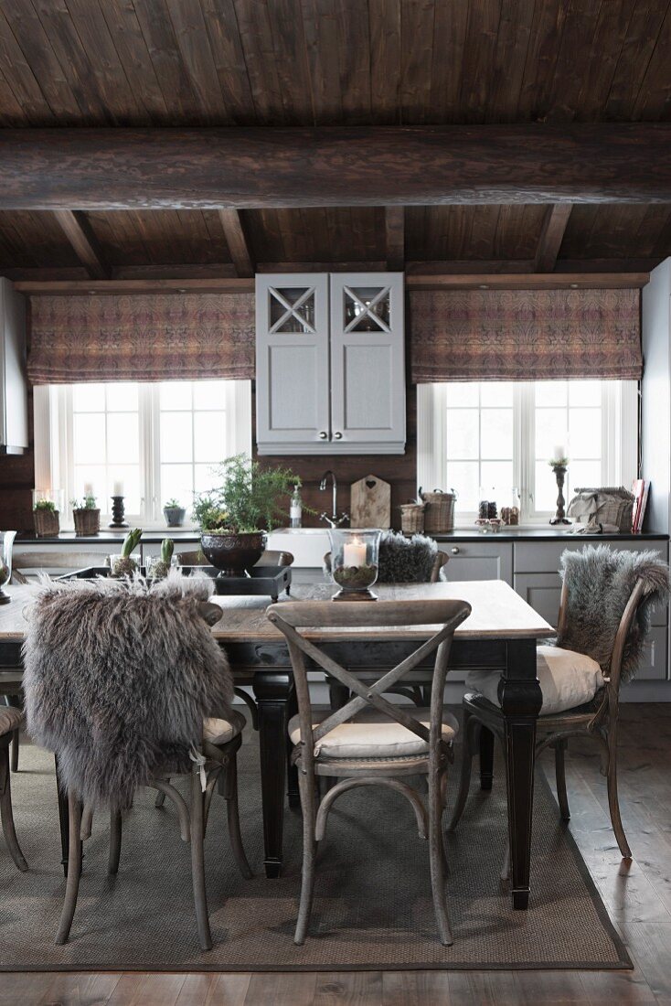 Rustikale Holzstühle teilweise mit Tierfell um Esstisch in ländlicher Küche eines Holzhauses