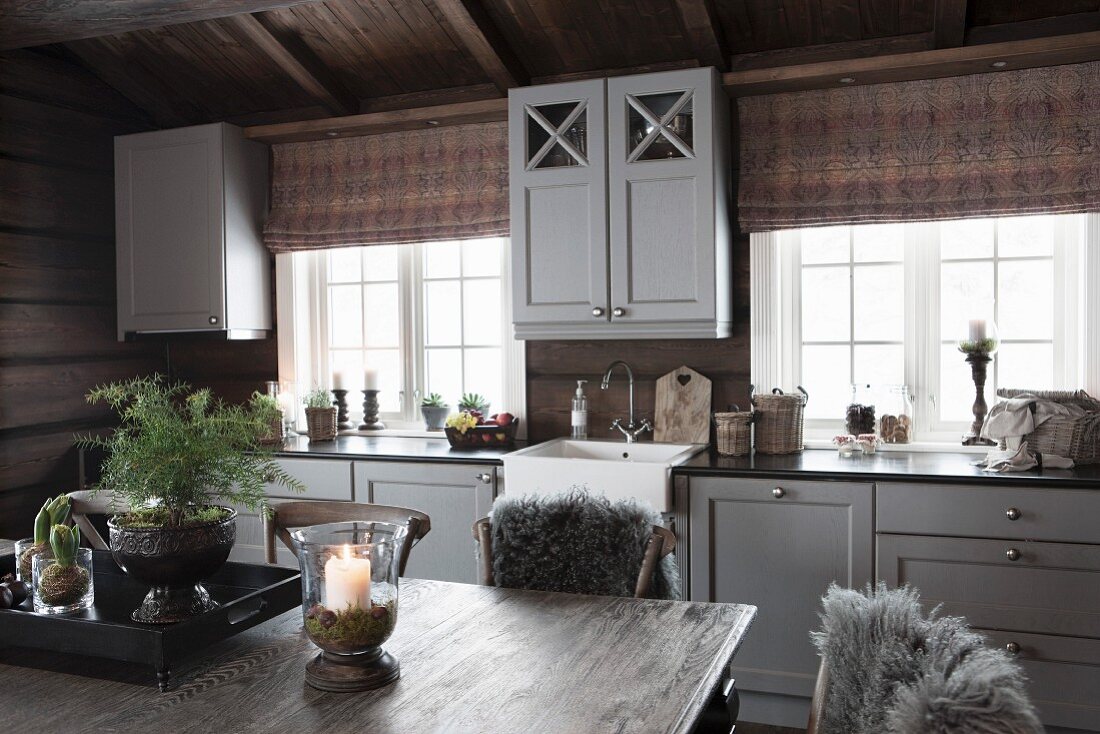 Blick über Esstisch auf Küchenzeile mit grau lackierter Holzfront in ländlichem Holzhaus
