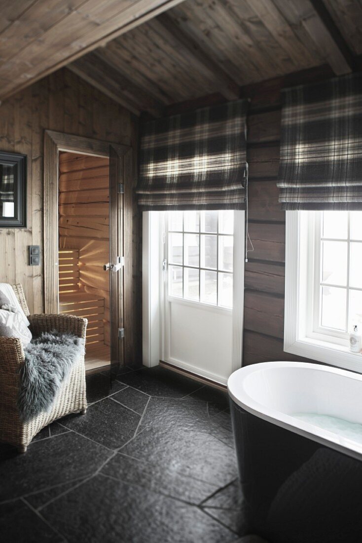 Bathroom with black slate floor, lattice windows, tartan roller blinds and view into sauna in background