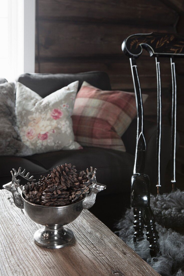 Tannenzapfen in Silberschale auf Holztisch, im Hintergrund Sofa mit Kissen