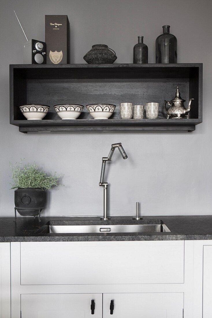 Küchenzeile mit eingebautem Spülbecken und moderner Armatur, oberhalb Wandbord an grau getönter Wand