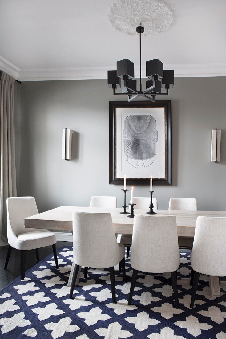 White-upholstered chairs around table with wooden top on patterned rug below pendant lamp with black cubic lampshades