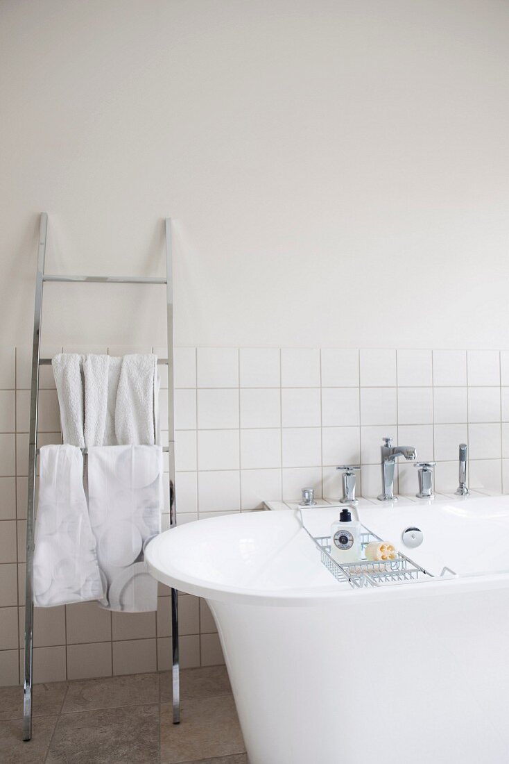 Free-standing bathtub next to stainless steel ladder-style towel rack