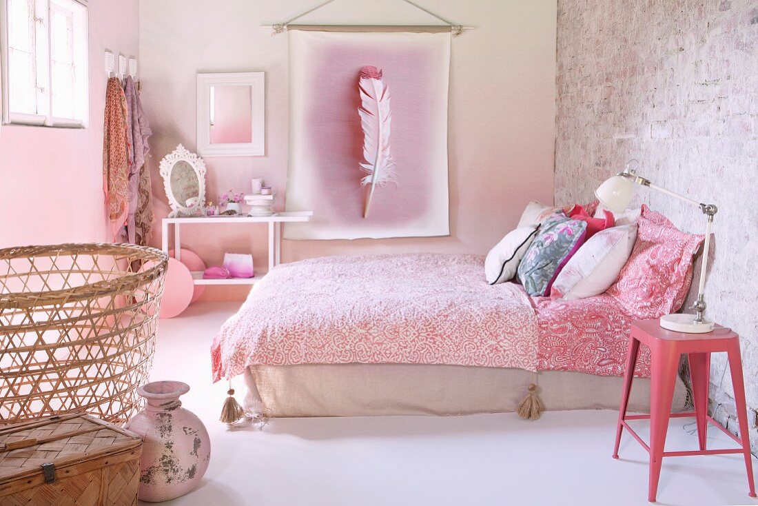 Schlafzimmer in Rosa mit Retro Flair, rosa Metallhocker neben Doppelbett mit gemusterter Tagesdecke, an Wand rosafarbenes Federmotiv auf Banner