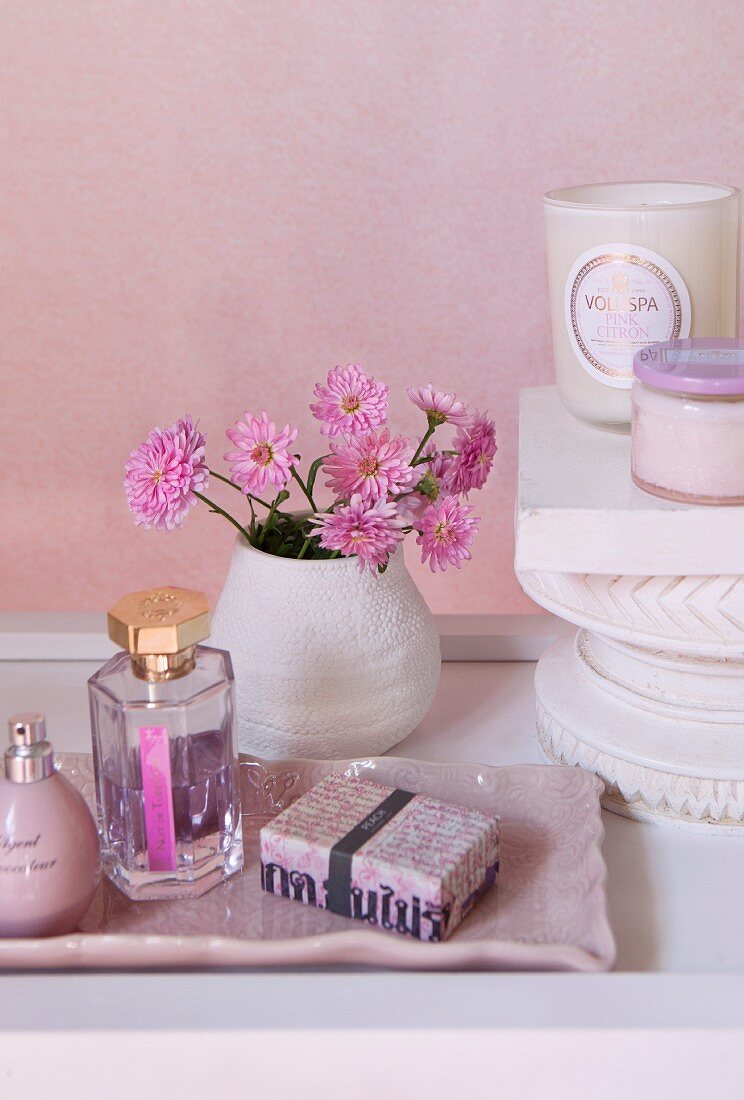 Kosmetikartikel auf rosa Schale vor Blumenstrauss mit pinkfarbenen Blumen