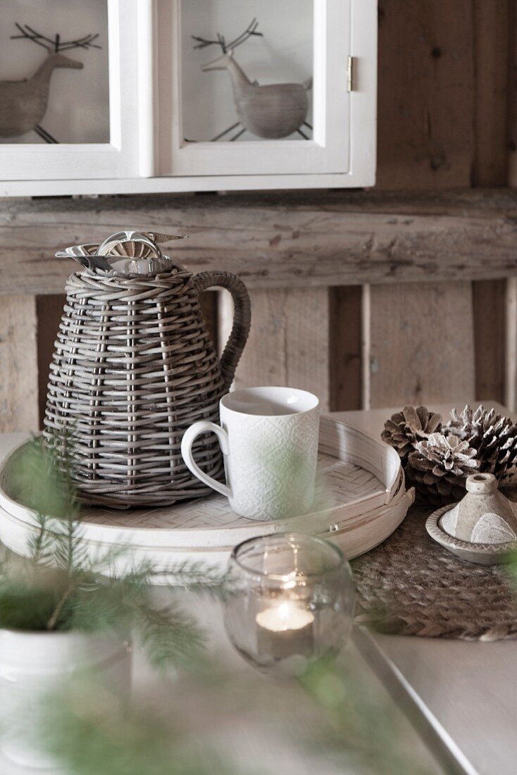 Thermoskanne mit Korbgeflecht und Kaffeetasse auf weißem Spankorb-Tablett auf weihnachtlich dekoriertem Tisch