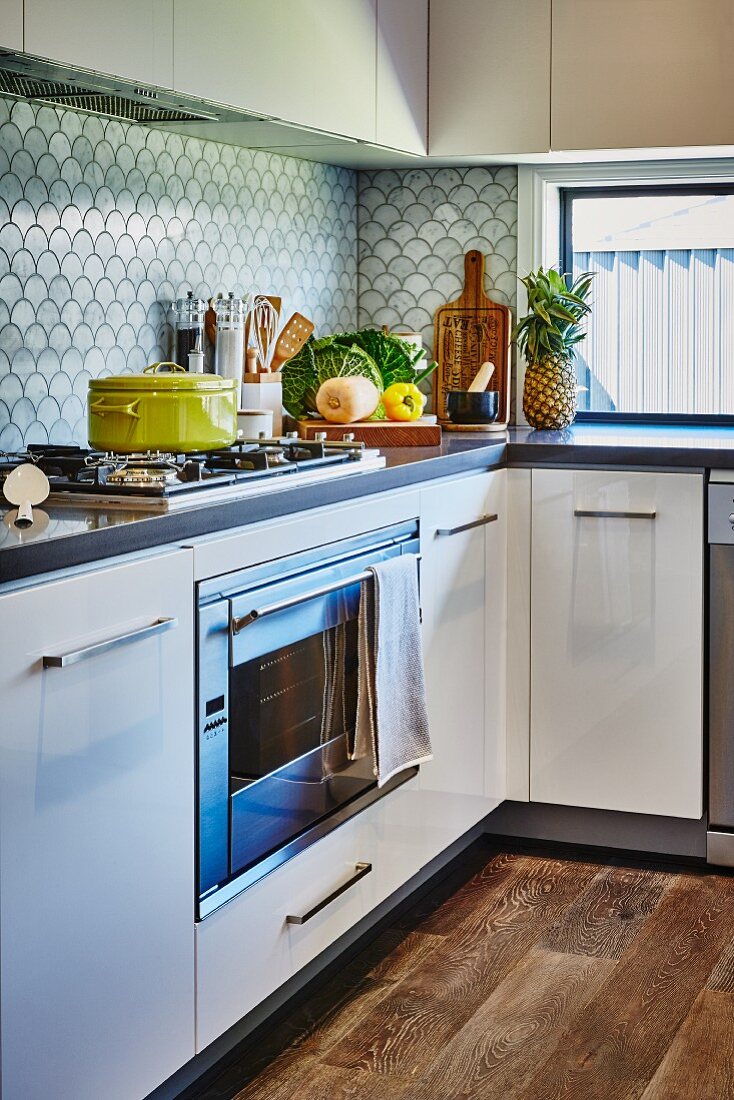 White kitchen with L-shaped counter, gas hob and splashback with fish-scale pattern