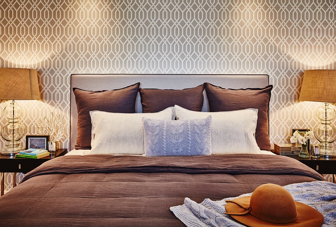 Kissen auf Doppelbett mit Polster Kopfteil an tapezierter Wand mit beigefarbenem Retro Muster