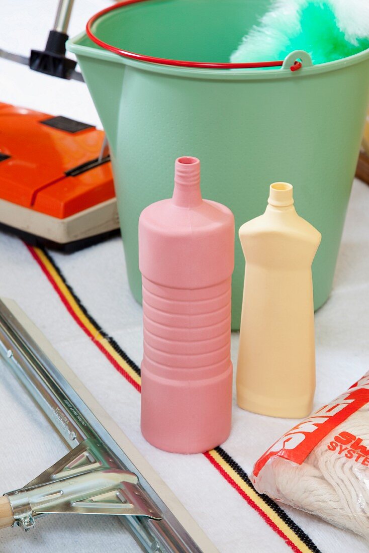 Pastel cleaning agent bottles, bucket and retro carpet sweeper on woven rug