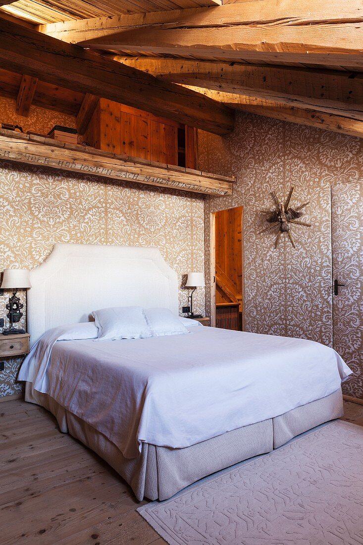 Floral gemusterte elegante Textilbespannung in Schlafraum unterm Dach mit Doppelbett in restauriertem Chalet