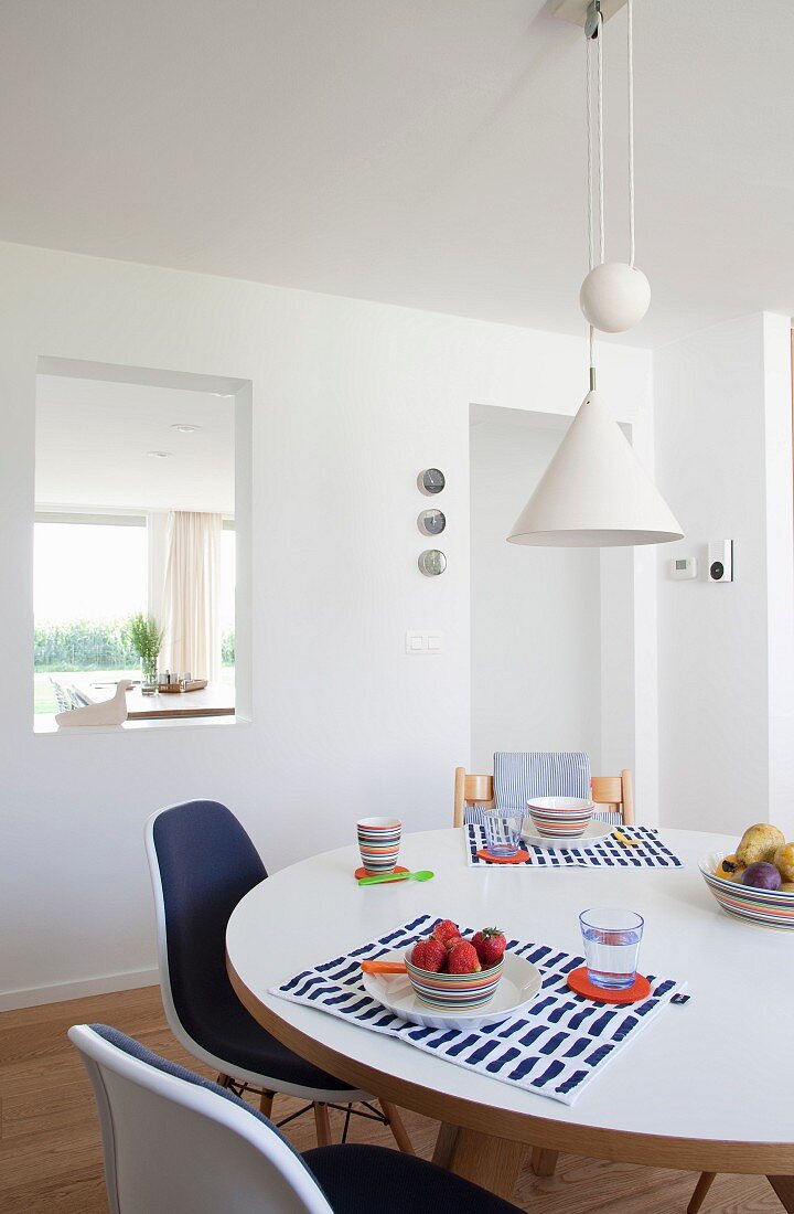 Schalenstühle im Klassikerstil um Esstisch mit Frühstücksgedecken, oberhalb weiße, verstellbare Pendelleuchte