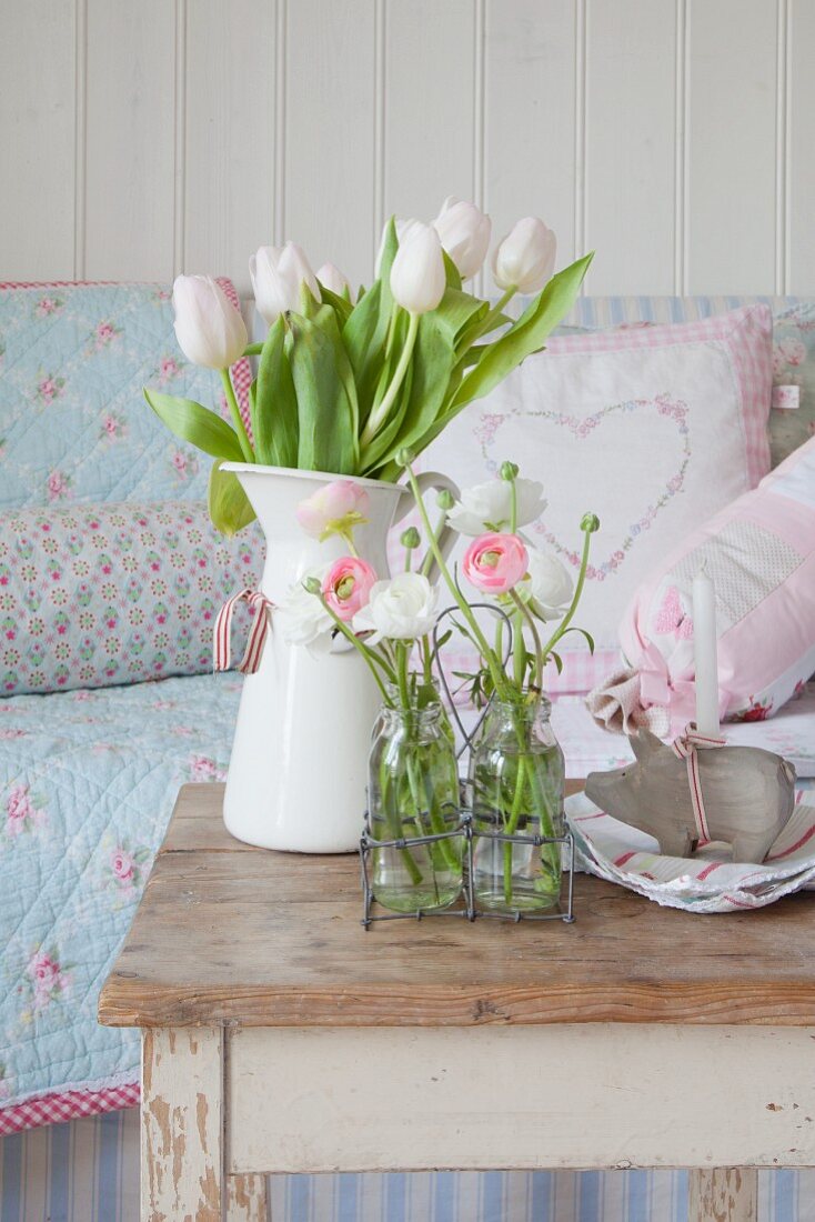 Tulpen und Ranunkeln in Emaillekrug und Glasflaschen als Frühlingsdeko auf altem Tisch