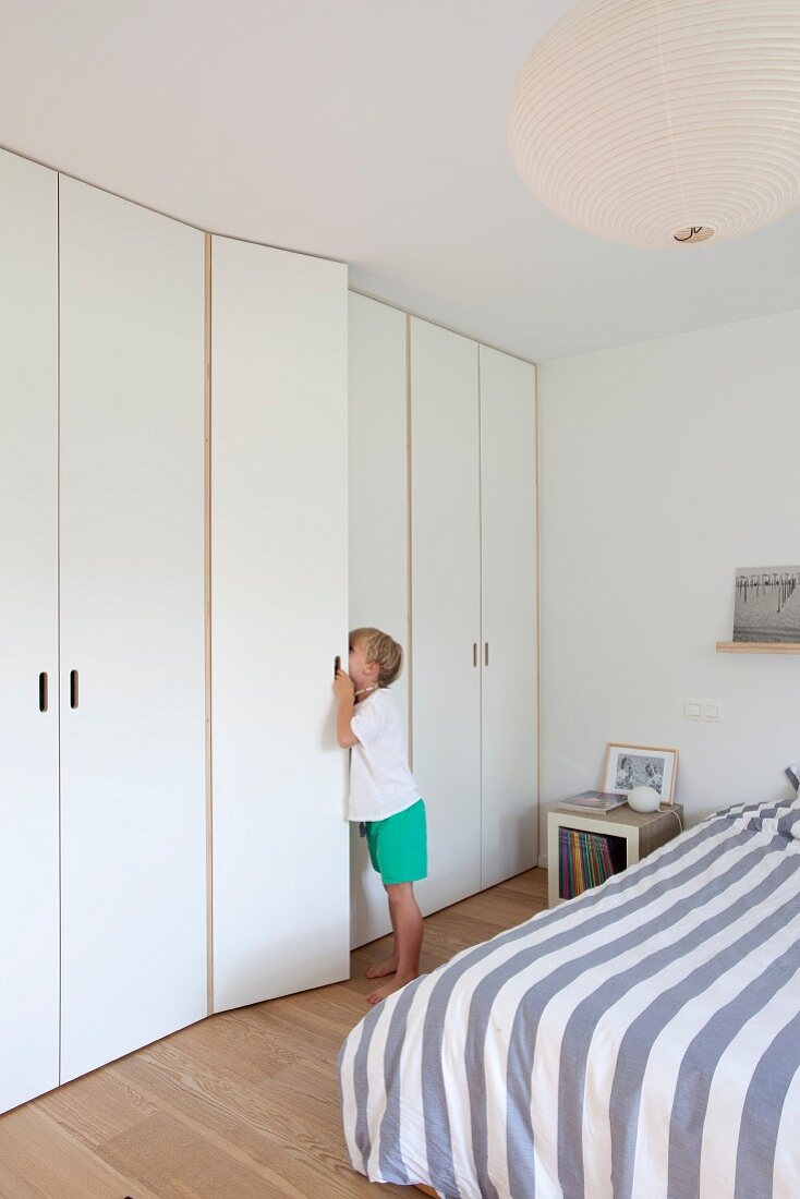 Boy peeping into white fitted wardrobe in modern bedroom