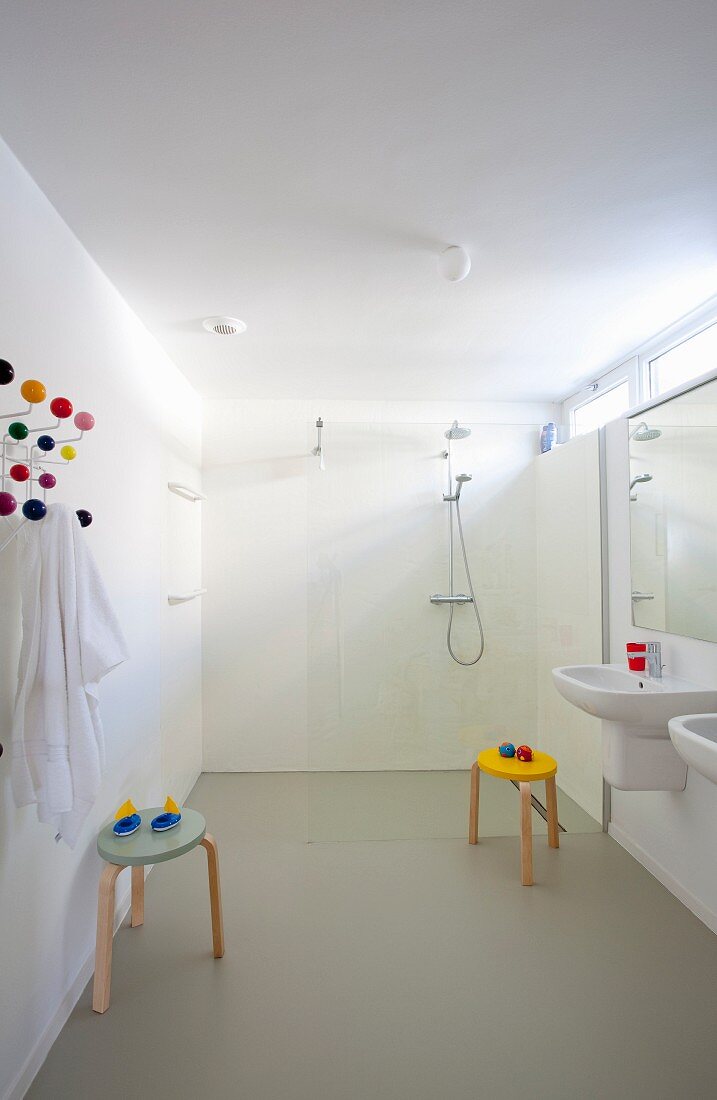 Grosszügiges Bad mit zwei Waschbecken, bunte Klassiker Hocker, vor bodenebenem Duschbereich mit Glastrennscheibe im Hintergrund