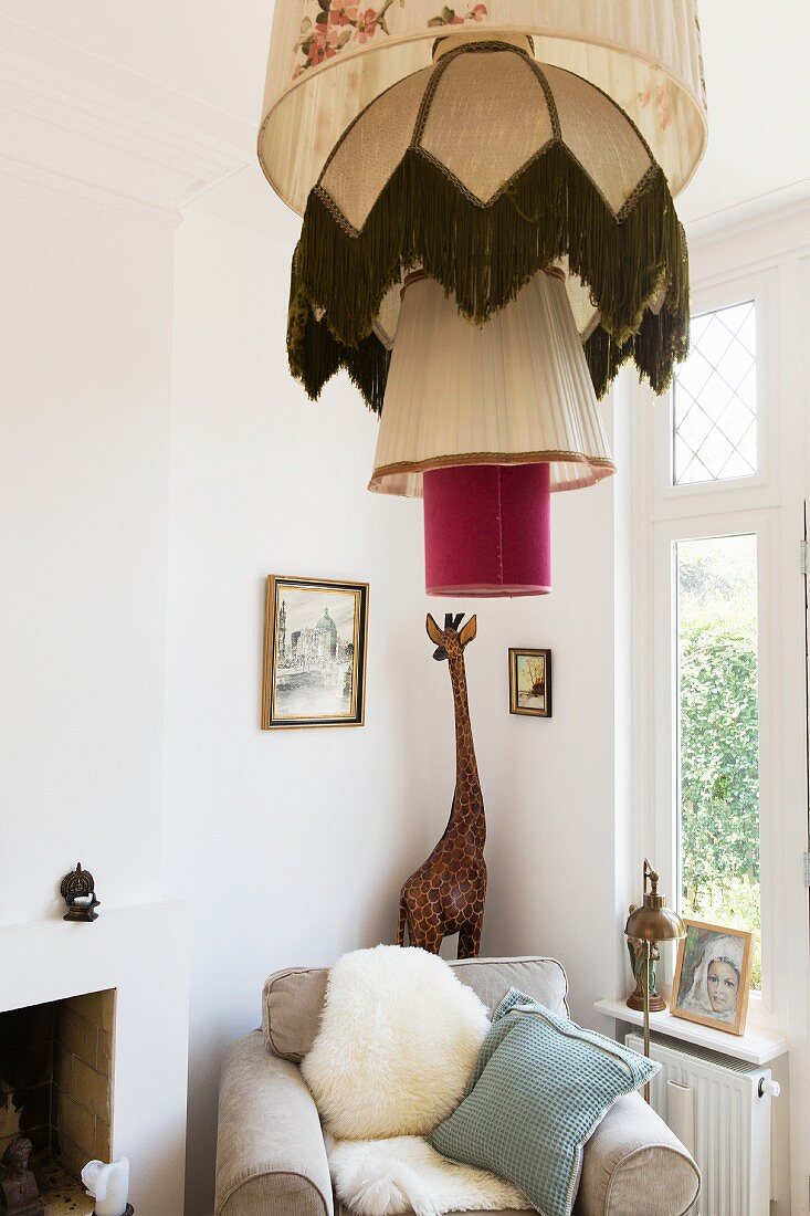 Pendant lamp with stack of retro lampshades in front of wooden giraffe and armchair with sheepskin in corner