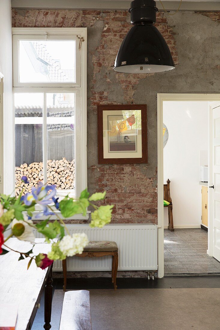 Bouquet on table, antique upholstered bench, modern radiator against unrendered brick wall and black industrial lamp