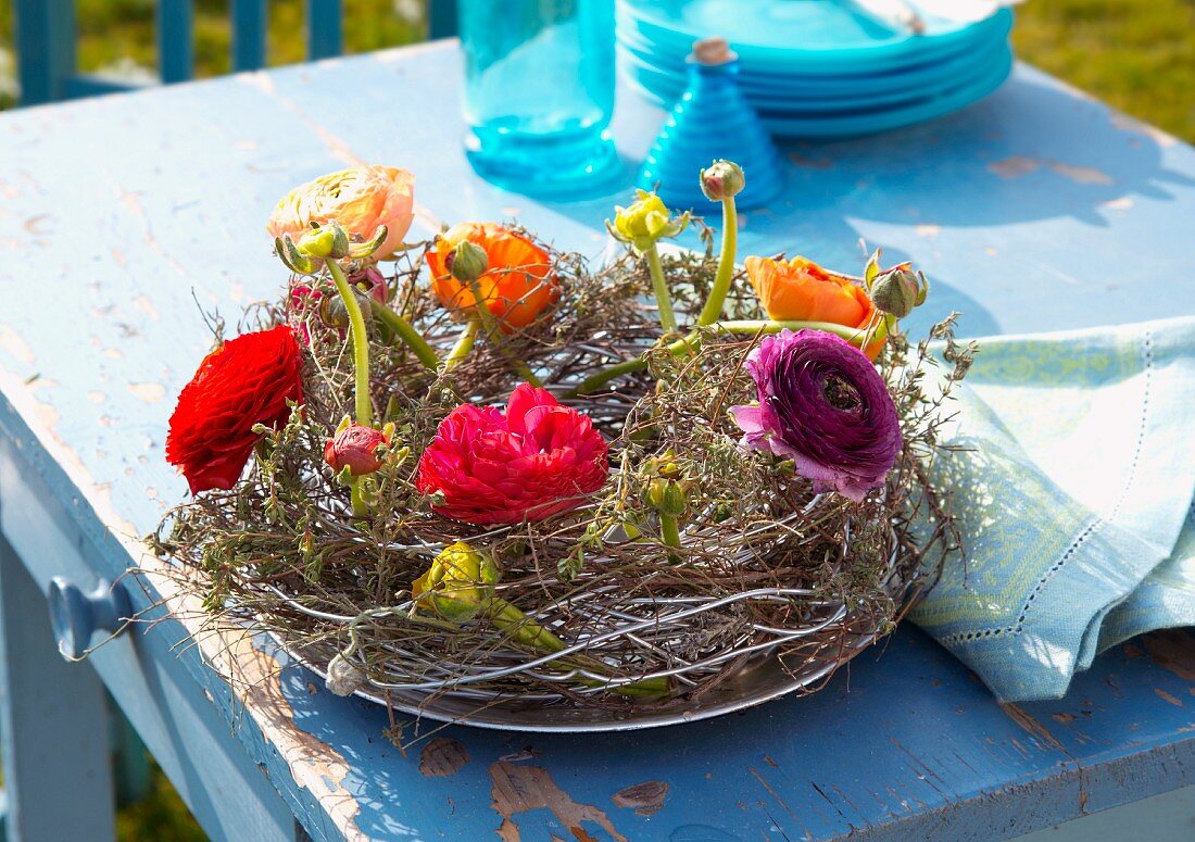 Wicker wreath with multicoloured ranunculus on garden table