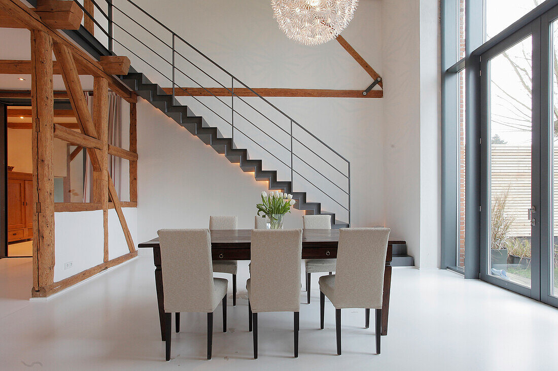 Dining table with chairs in a modern home with wooden beams and staircase