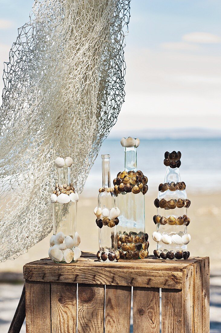 Glass bottles decorated with seashells on wooden crate on beach