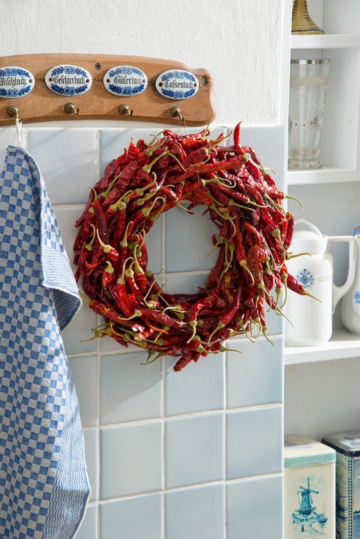 Wreath of dried red chilli peppers hung from wall hooks in kitchen