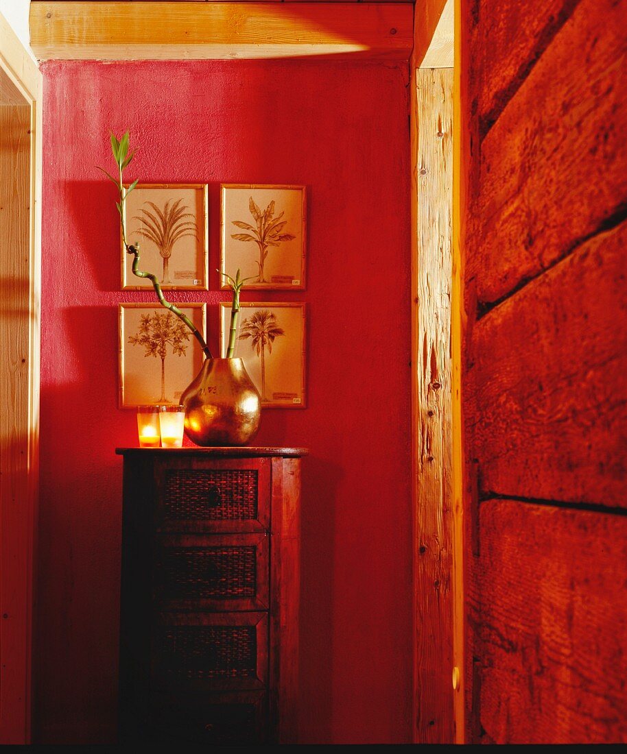 Metal vase of bamboo twigs and tealight holders on cylindrical chest of drawers against red-painted wall