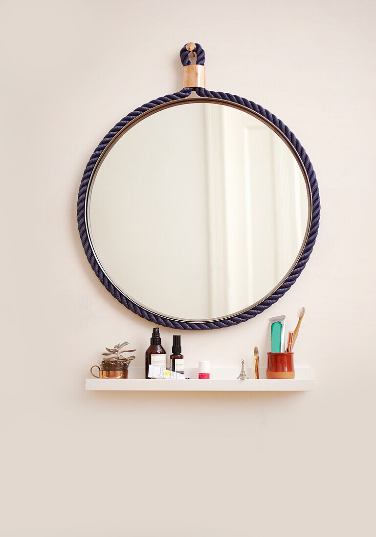 Round mirror with blue rope frame over floating shelf in the bathroom