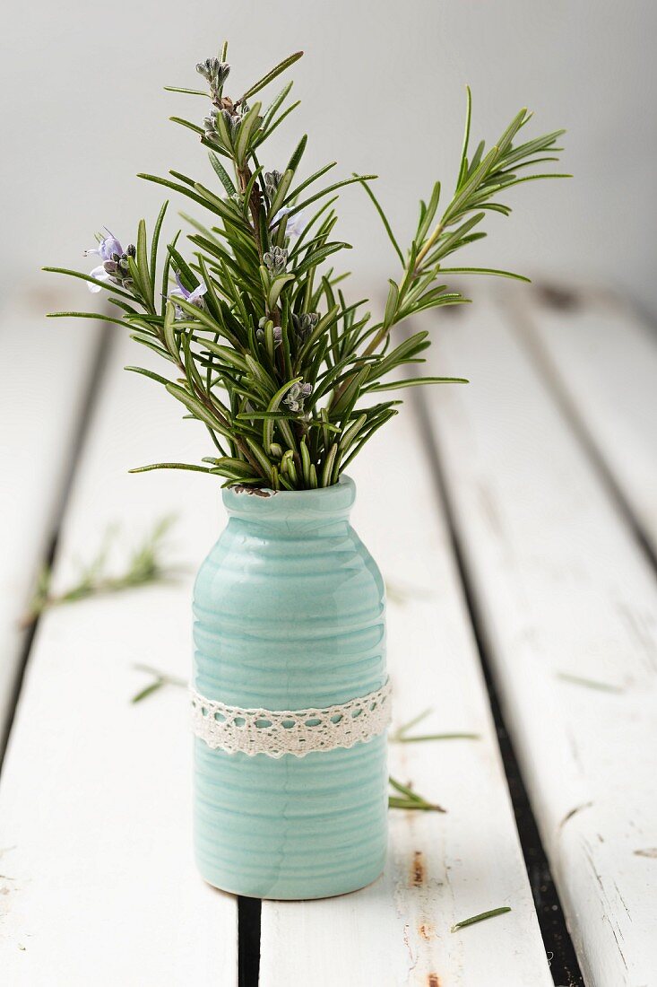 Blühende Rosmarinzweige in Vase mit Spitzenborte
