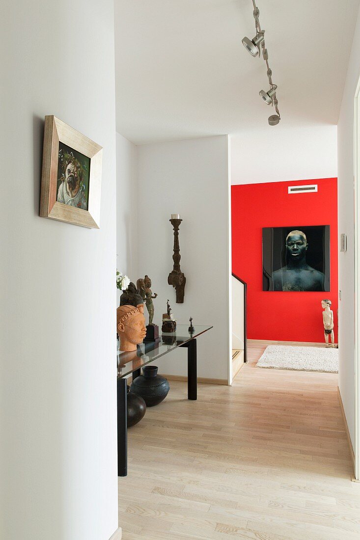 Moderner Gangbereich, in Nische Ausstellungsobjekte auf Tisch, im Hintergrund Foto Portrait an rot getönter Wand